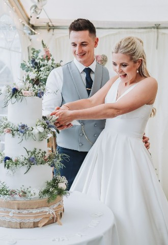 Bride & Groom cutting their 3 tier white wedding cake with floral decorations at The Stables Wedding Farm in Oldham