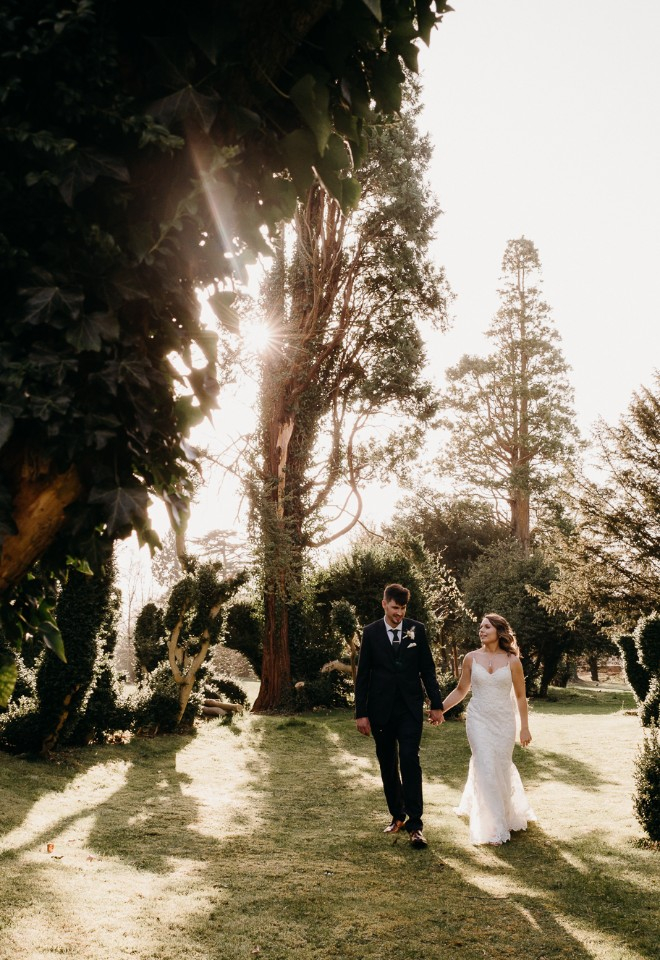 Bride and groom walking hand and hand in the Oakley Hall topiary gardens.