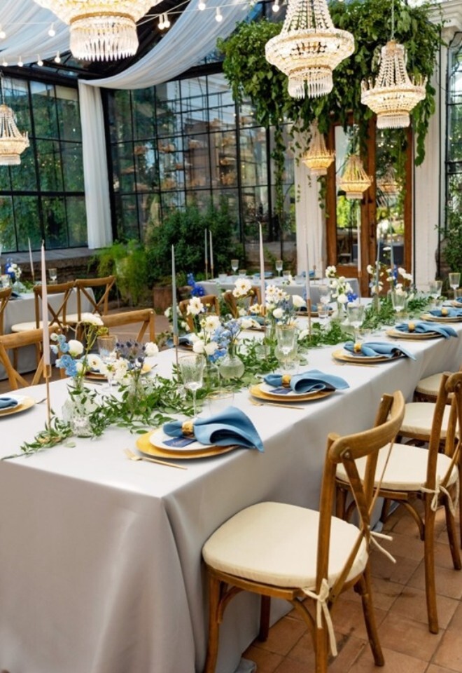 Orangery table with hanging lights, green centre piece flowers and blue napkins