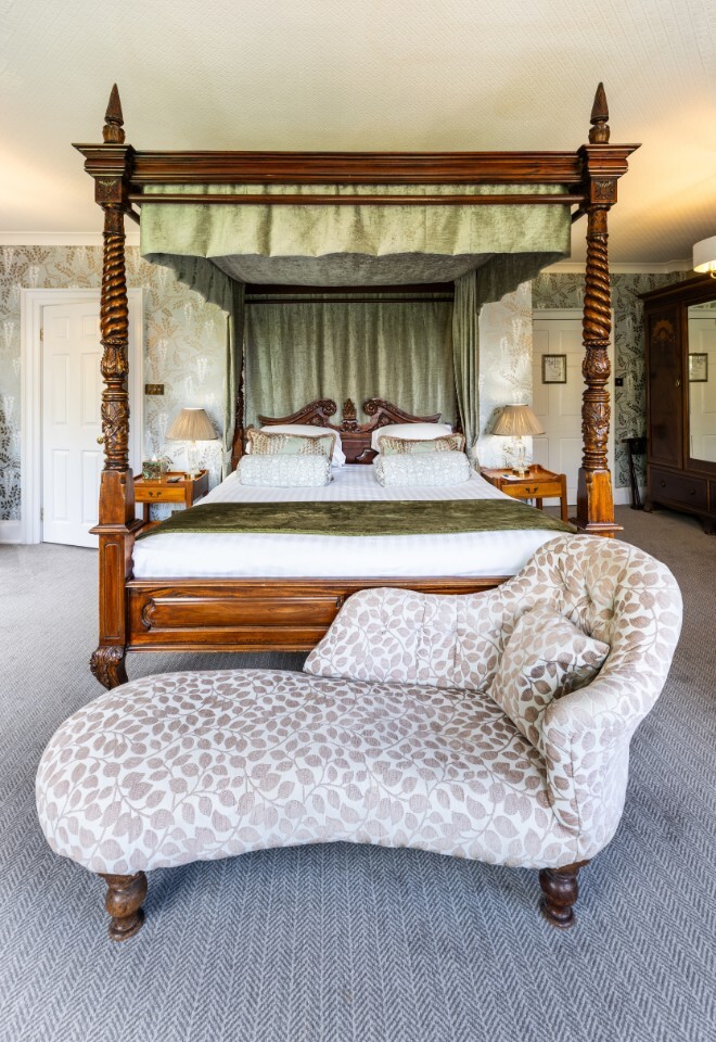Bridal suite at Washingborough Hall Hotel featuring a grand four-poster bed with carved wood, soft green drapes, and a patterned chaise longue in front.