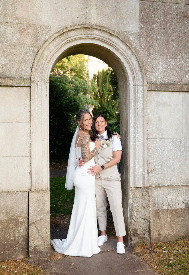 “Couple posing together in an archway at Christchurch Priory in Dorset during their wedding photographed by Katy Brothers Wedding Photography”