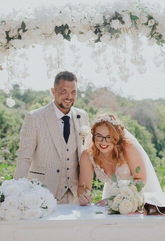 bride and groom signing the register surrounded by a flower arch