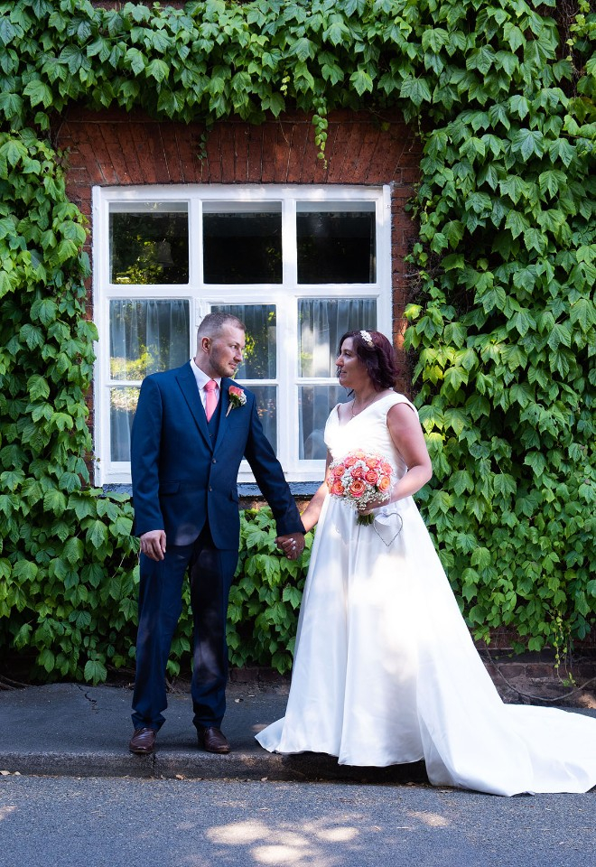 Bride and Groom gaze at each other on wedding day in Birstall Leicestershire backed by creeping plants and red front doors