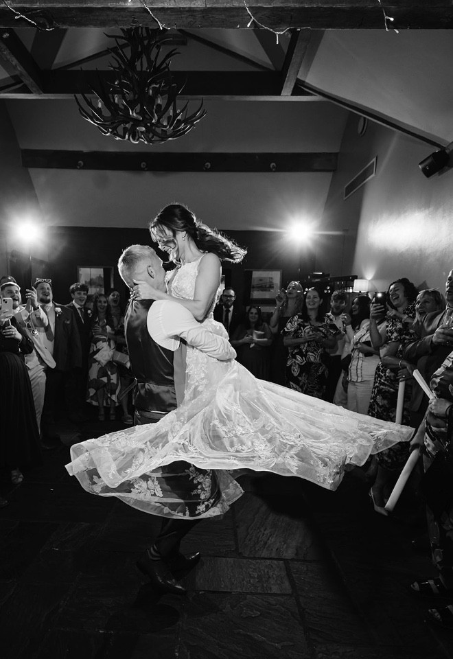 Groom lifting the bride during their first dance, surrounded by wedding guests at The Cock O’Barton