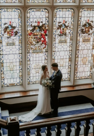 Bride and Groom stood in front of stain glass windows at Easthampstead Park