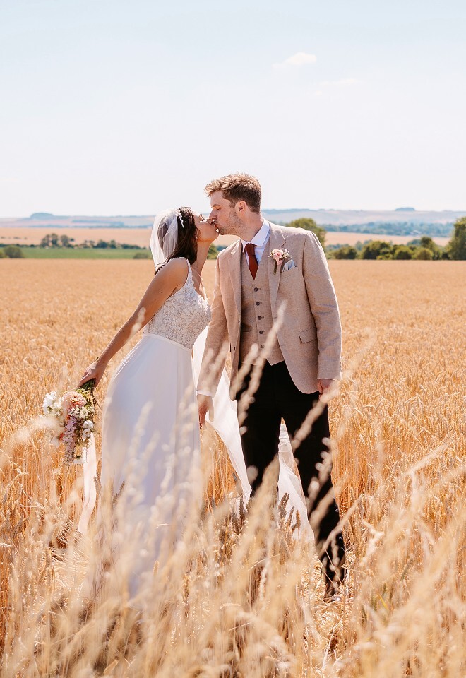 Relaxed bride and groom kissing in the Cotswolds countryside, with natural daytime wedding portraits