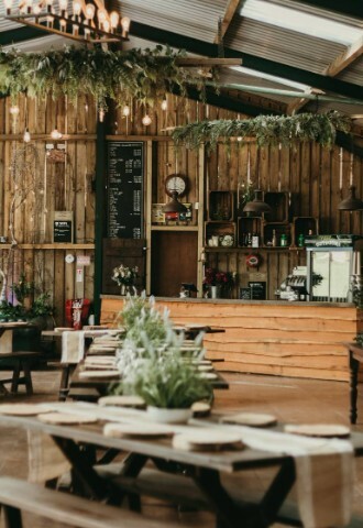 Interior of barn, Tables set up with runners, log splits and centrepieces. In the background there is a fully stocked bar