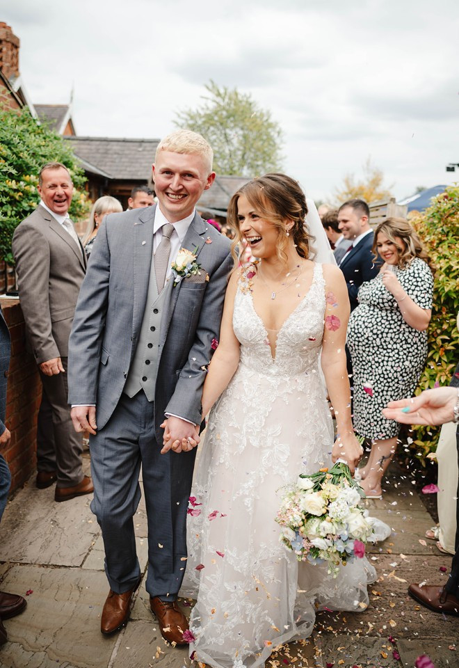 Newlyweds walking hand in hand through colourful confetti at The Cock O’Barton.