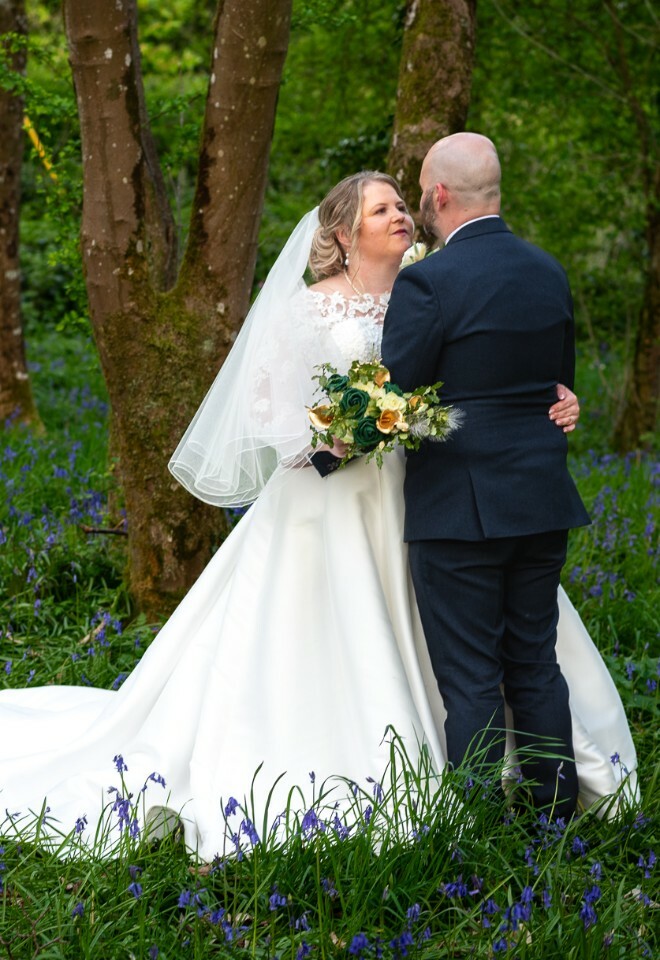 A couple shares an intimate moment in a woodland setting filled with blooming bluebells on their wedding day.