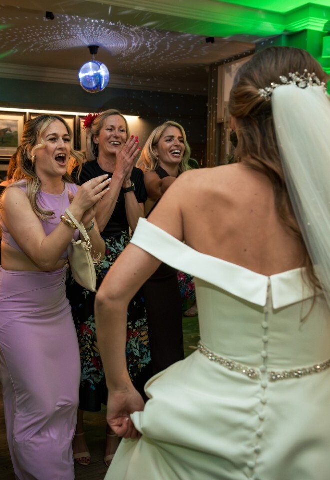 Bride dancing with guests at Washingborough Hall Hotel, surrounded by friends in colourful dresses under green lighting and a disco ball at the evening reception.