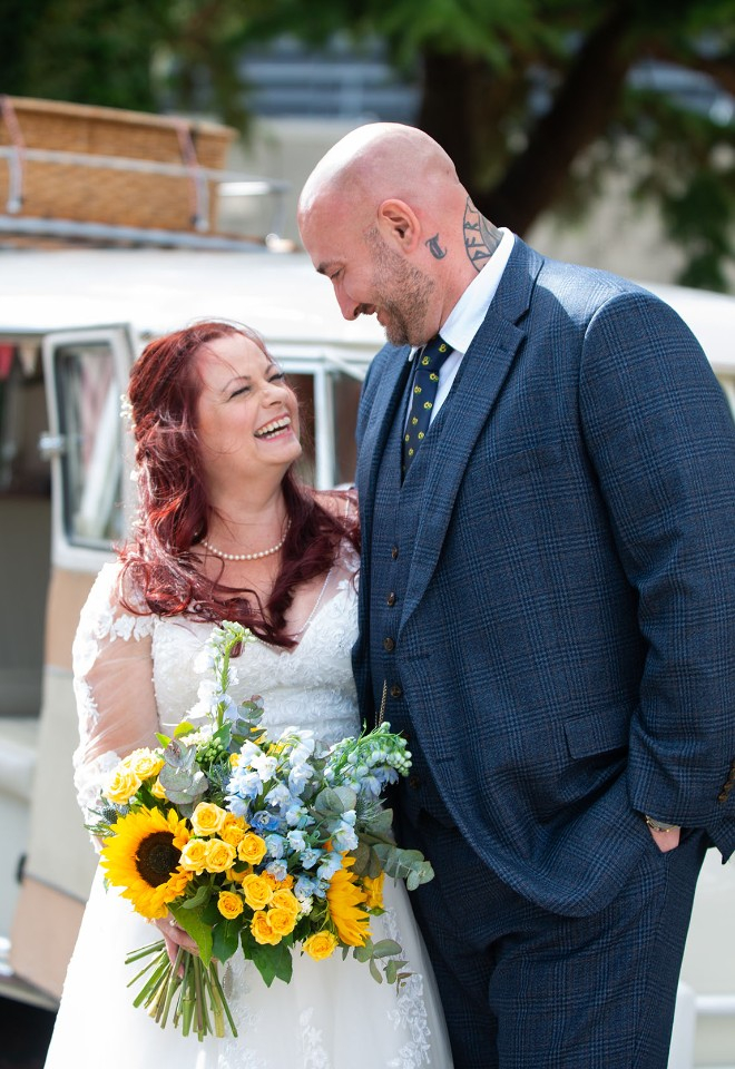 Tall groom smiles down at his bride holding a bouquet of sunflowers in front of a VW Camper at Leicestershire County Hall Registry Office