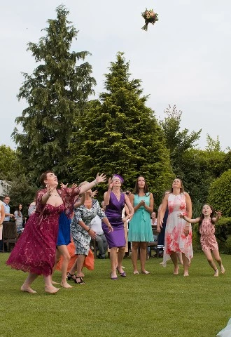 Bride throwing bridal bouquet of flowers to the female wedding guests and bridesmaids