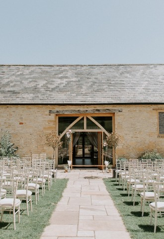 Outdoor wedding ceremony with Upcote Barn as the backdrop