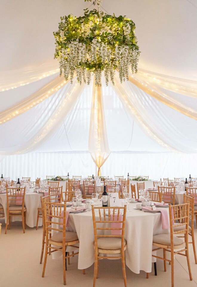 Romantic white drapes and linings for a barn transformation, with a wisteria chandelier and pink accents on round dining tables