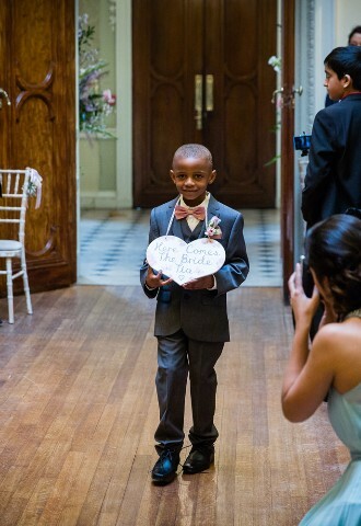 Page boy walking down the Aisle with sign saying "Here comes the bride"