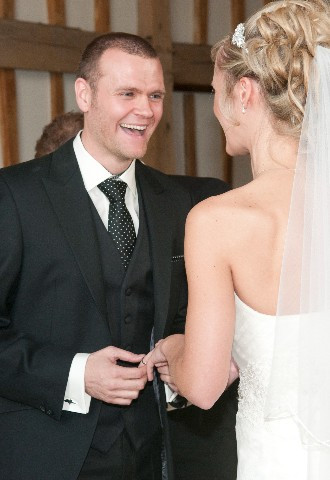Brides and groom exchange wedding rings with smiles and laughter during wedding ceremony