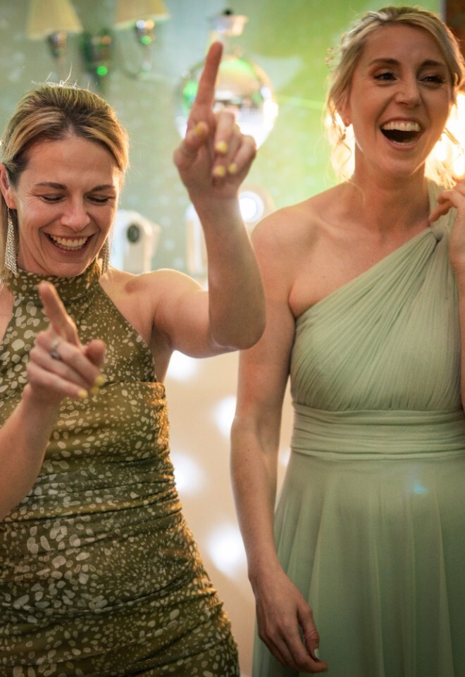 Guests dance and laugh under disco lights at Washingborough Hall Hotel, with two women in sage green dresses and one in a patterned gold dress enjoying the celebration.
