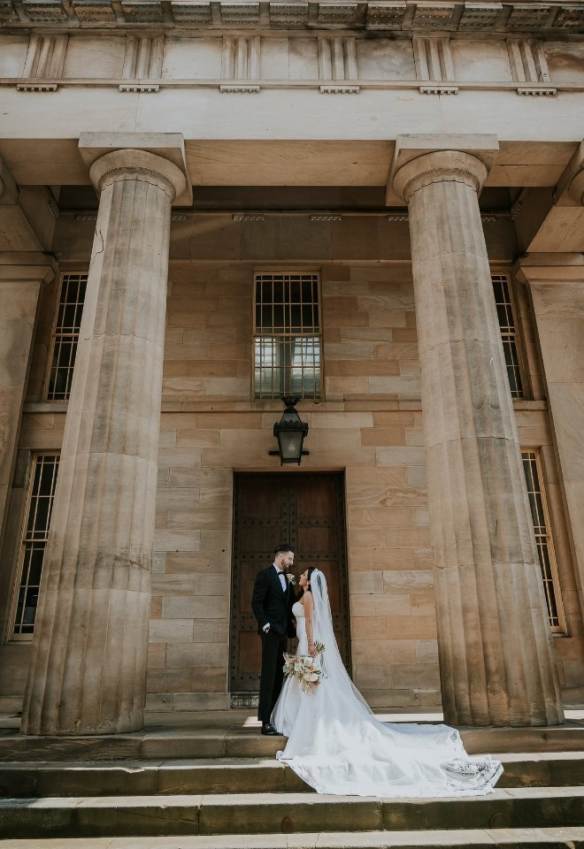 Bride and groom standing in front of the pillars at the Vermont Hotel in Newcastle