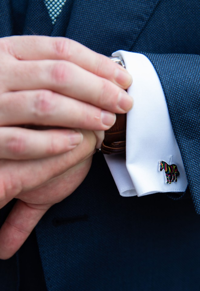 Close up of hands and wrist as a groom checks his watch. Cufflinks are brightly coloured zebras