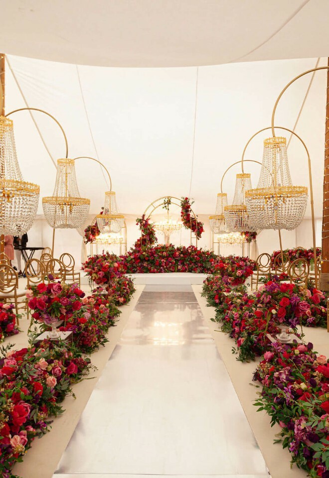 Stunning luxury marquee for an Asian wedding with red roses bordering a mirrored aisle and handing chandeliers
