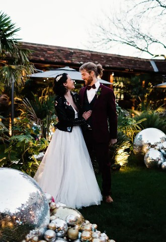 bride and groom pose outside in the christmassy gardens of the crazy bear stadhampton, oxfordshire
