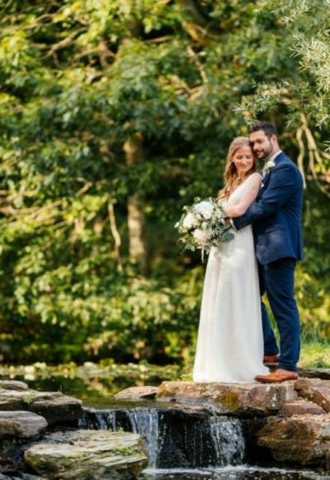 Couple standing together on the waterfall with the wooded area behind them- Sprowston Manor Norwich