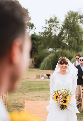 A groom looks at his bride as she walks up the aisle of a countryside wedding