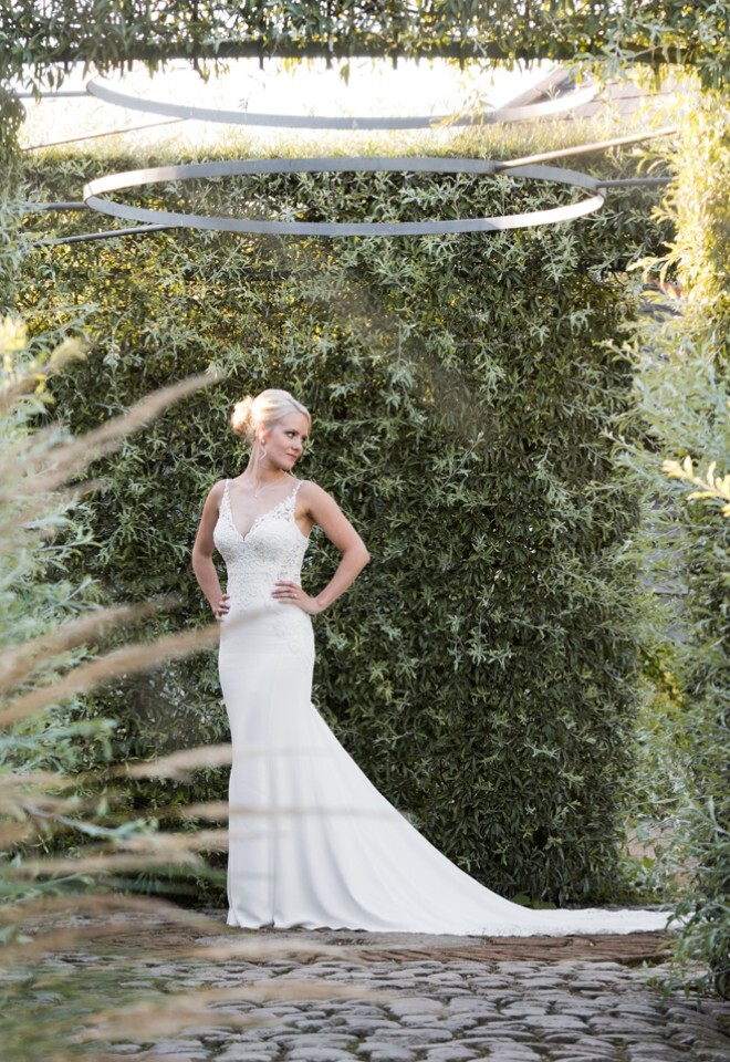 Bride standing alone with hands on hips looking away from the camera in the gardens of Bury Court Barn Surrey