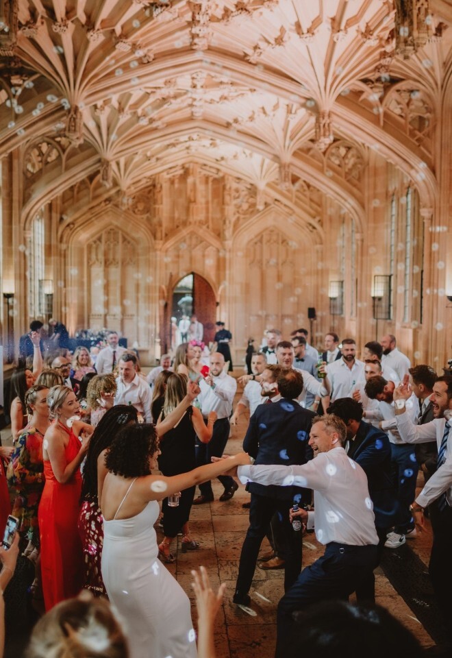 Lively wedding reception with guests dancing beneath the grand vaulted ceiling of the Bodliean Library wedding venue, taken by V & H Photography.