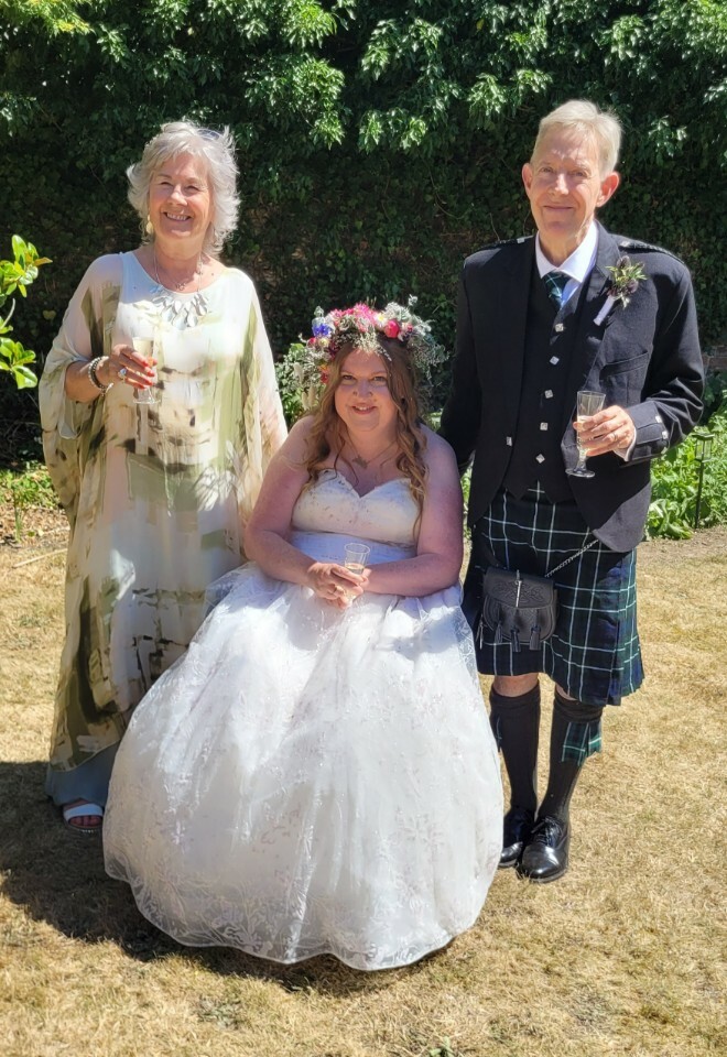Suffolk celebrant dress in a silk green dress with a bride and groom after their ceremony. Bride has a beautiful flower crown on her head