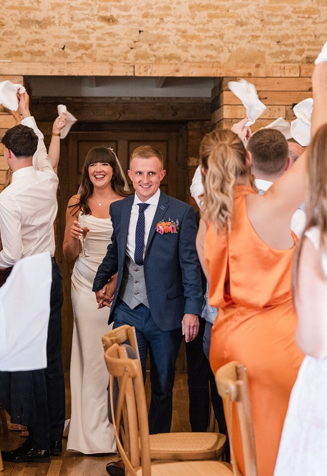 A bride and groom walking across the barn for their wedding breakfast at an Oxfordshire wedding venue