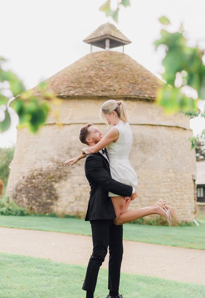 Groom lifting bride in front of dovecote