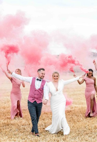 Wedding party holding pink smoke bombs to match bridesmaids and groomsmens outfits.
