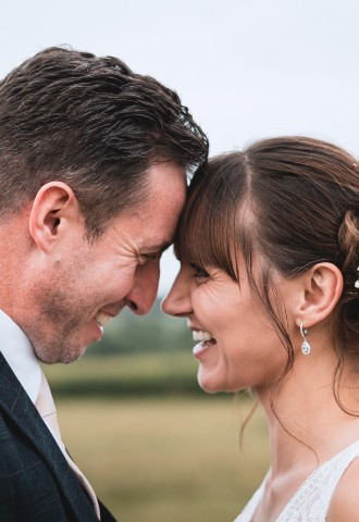 A bride and groom touch foreheads and laugh while looking in to each others eyes