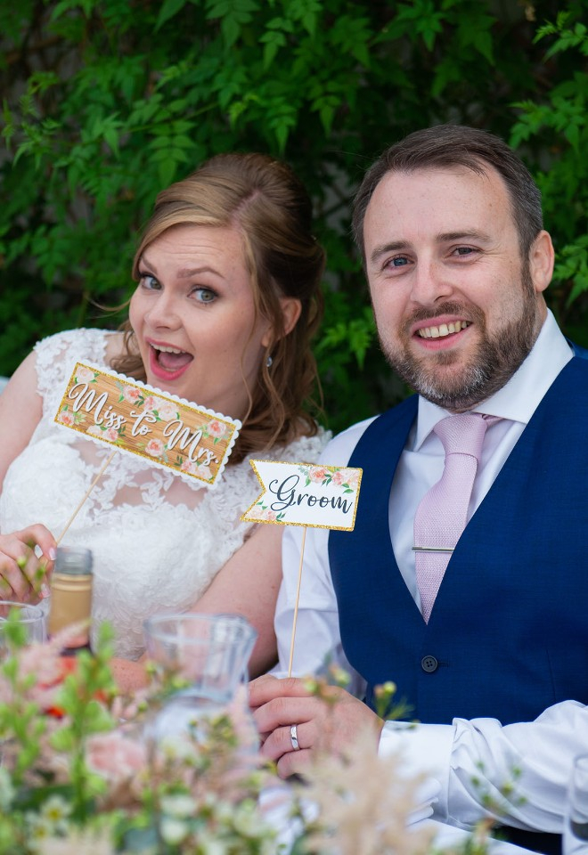 Fun newlyweds holding bride and groom signs up whilst seated at the top table on their wedding day at Sutton Bonington Hall Leicestershire
