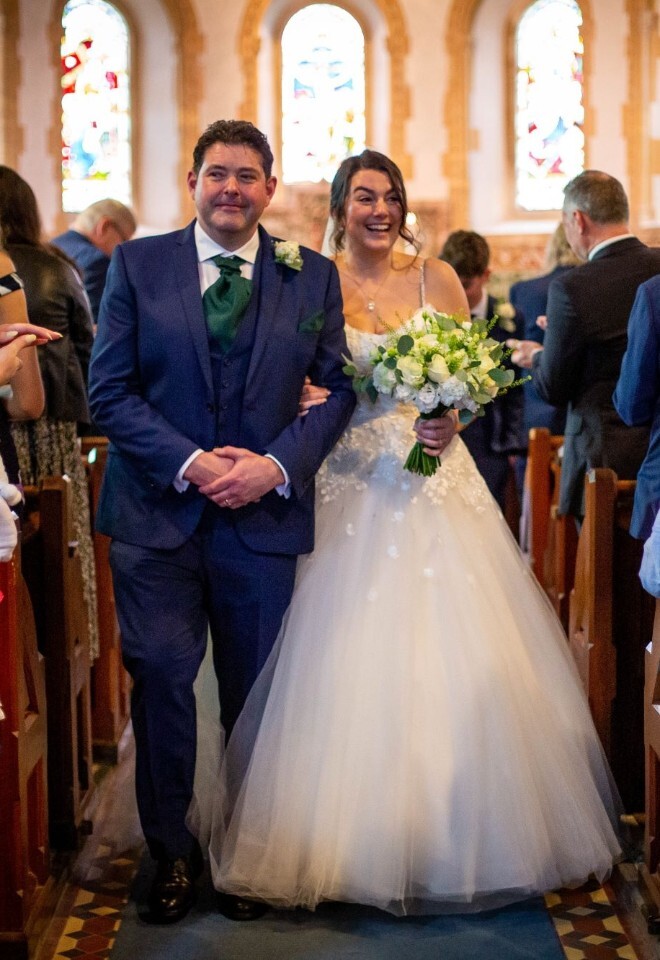 Bride and groom walking back down church aisle after ceremony with wedding florals in Somerset by FLOWERS BY ANYA