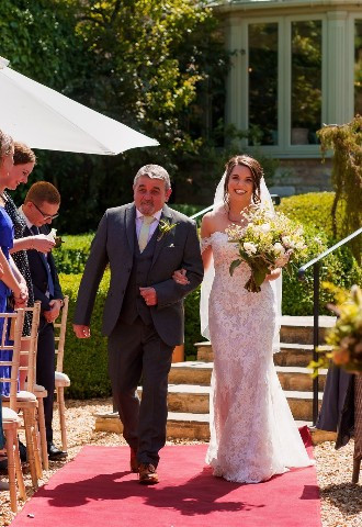 Bride and her father walking down the aisle at her outdoor wedding ceremony at The Bay Tree Hotel, Burford, Oxfordshire