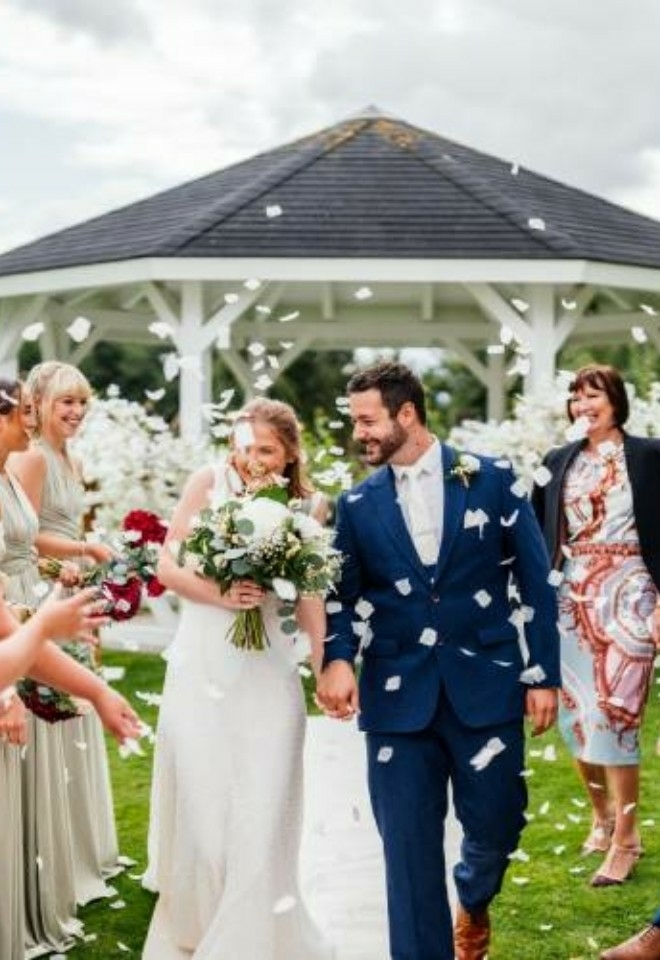 Couple walking down the aisle whilst guests throw confetti, outside pagoda- Sprowston Manor Norwich