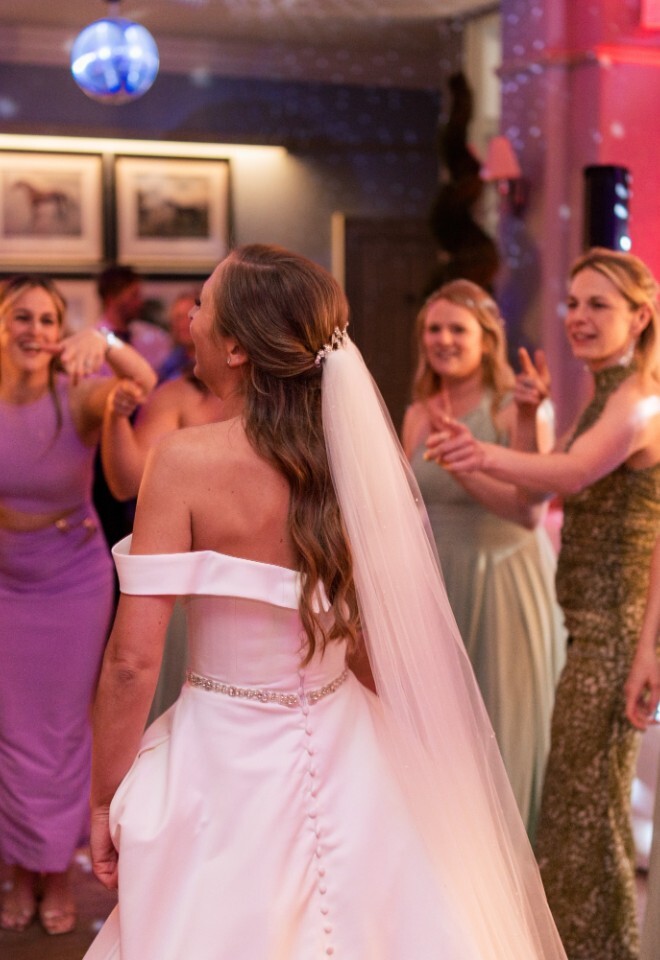 Bride dancing with guests at Washingborough Hall Hotel, surrounded by friends in colourful dresses under pink and purple lighting with a disco ball overhead.