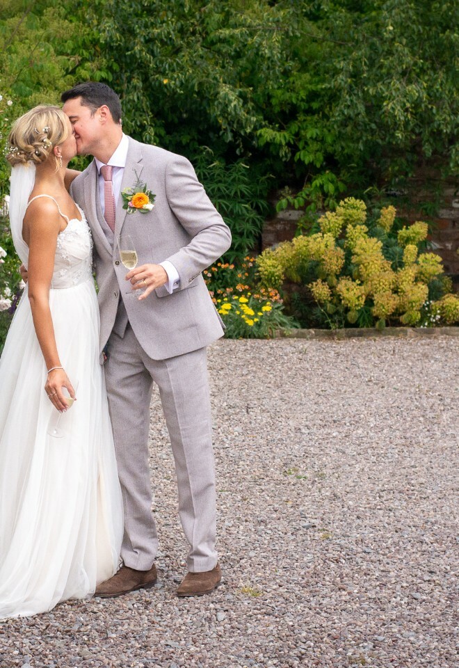 Newlyweds share intimate moment in garden surrounded by colorful wildflowers and greenery.