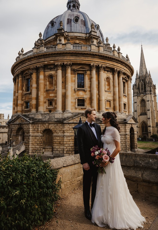 Wedding couple stands in Exeter college in oxford overlooking Radcliffe square
