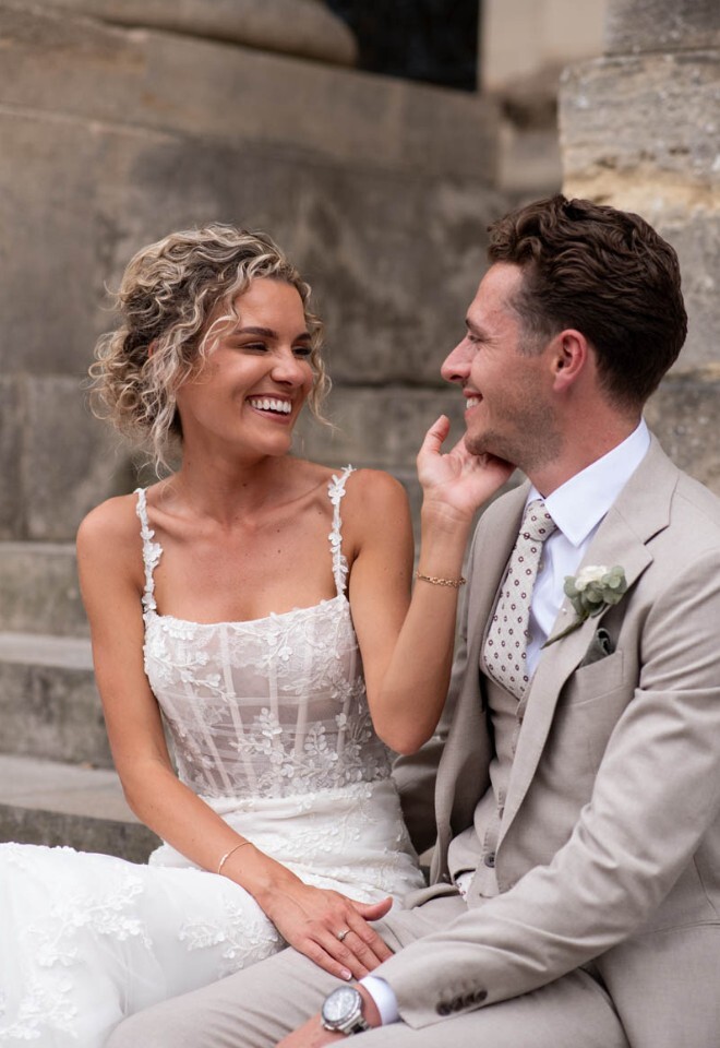 Bride and groom smile at each other sat on steps outside the Bodleian Library.