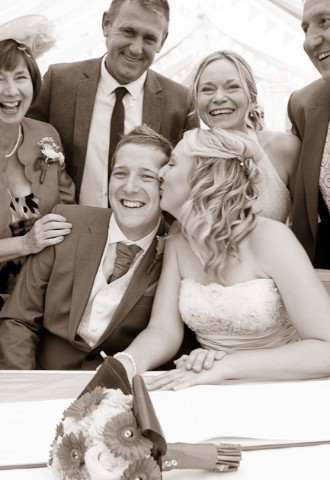 Bride kisses groom after signing the wedding register surrounded by happy family