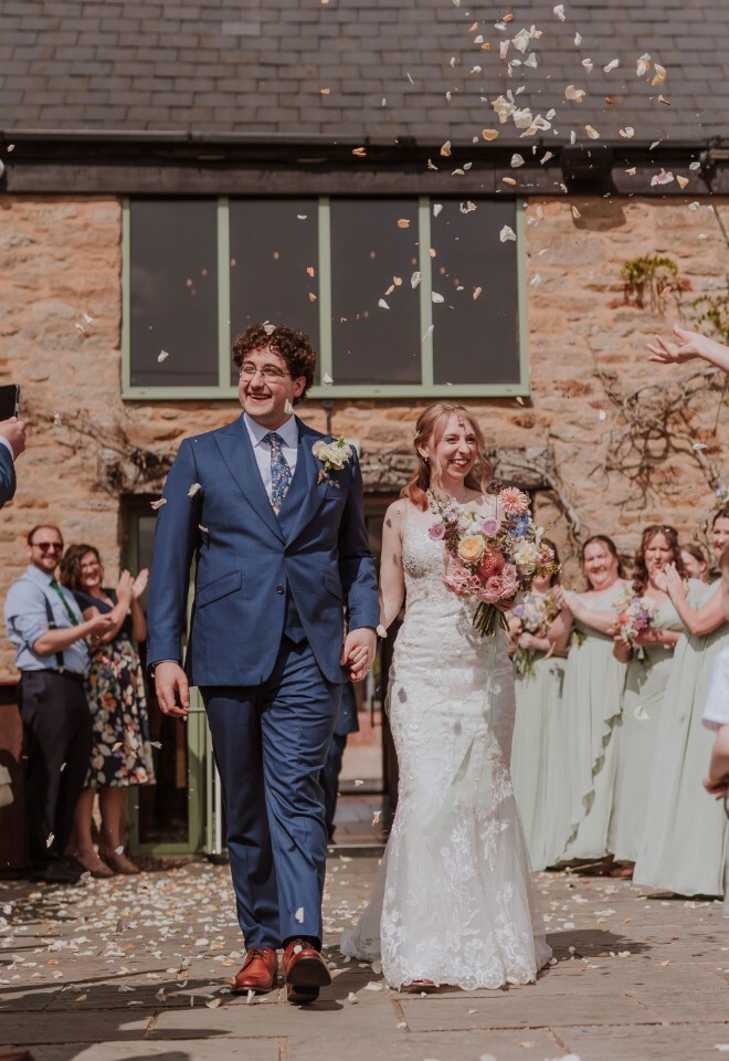 A bride and groom walking through confetti at an exclusive Oxfordshire wedding venue