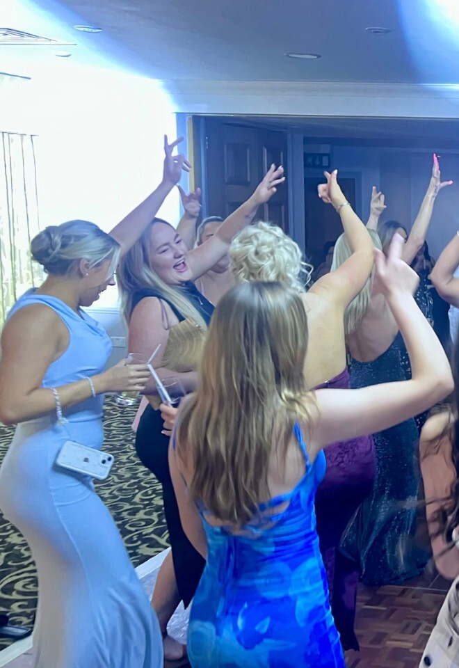 A lively wedding reception crowd dancing on a wooden dance floor, with guests raising their hands and celebrating under cool blue event lighting.