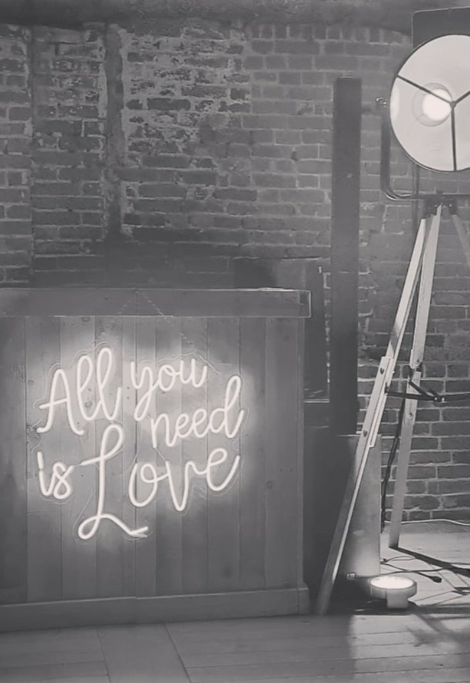 Wooden dj booth with all you need is love in light up letters on the front and 2 large lights either side