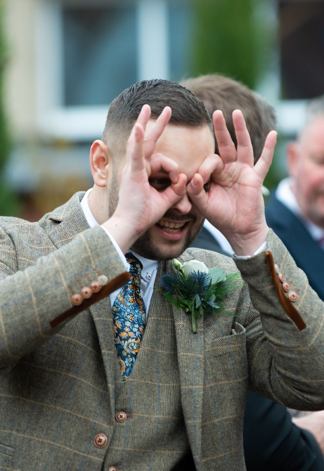 A wedding guest makes owl eyes with his fingers over his face at his mothers wedding