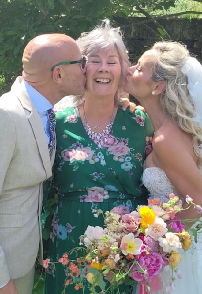 A very happy Norfolk celebrant dressed in a green dress being kissed by the bride and groom after their wedding ceremony