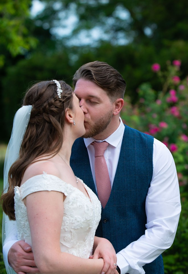 Bride and groom kiss in front of a stunning bush of hot pink flowers in the grounds of Norwood Park, Southwell