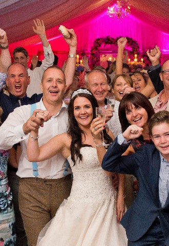 Bride and groom with wedding guests on the dance floor cheering and laughing 